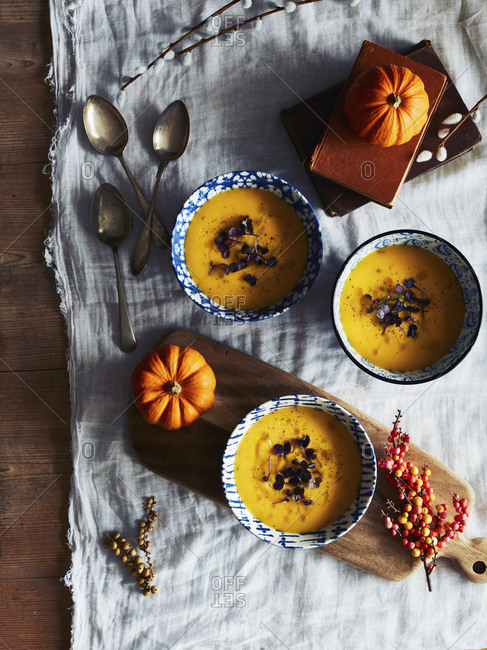 High angle close up of orange pumpkins and bowls of pumpkin soup on a table.