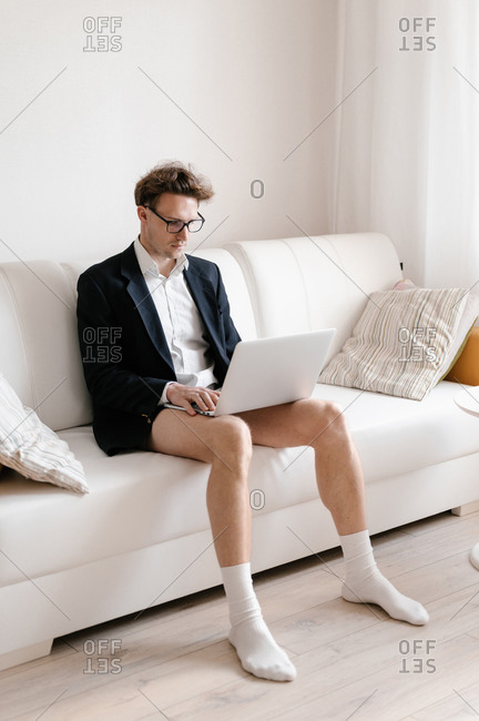A man works from home on the couch in his jacket and underwear