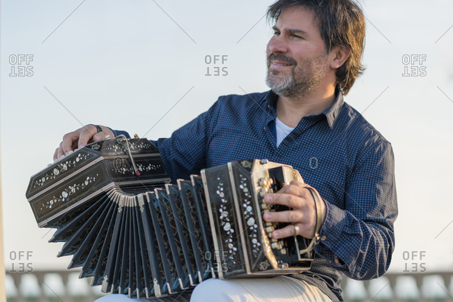 Happy senior male musician playing accordion while looking away