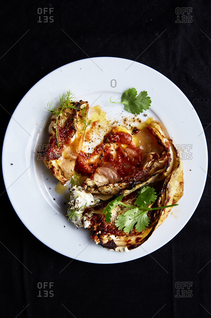 Cabbage roasted in tomato puree served on a white plate on a dark background,