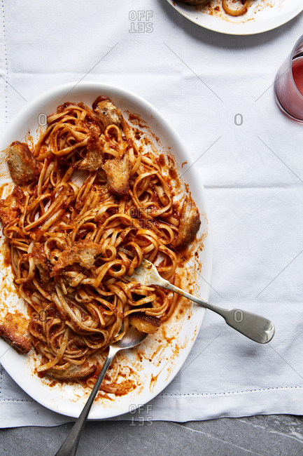 Fresh pasta in a tomato sauce with croutons and a glass of wine on a white linen cloth,