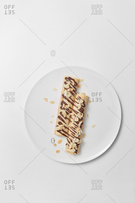 Freshly cooked homemade sweet spring rolls with filling inside and top from chocolate and almond chip on a ceramic plate and light grey background, copy space. Top view.