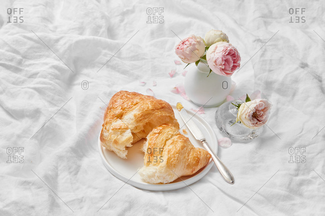 Morning wonderful still life from freshly baked homemade delicious sweet croissant and small ceramic vase of aromatic roses flowers on a crumpled textile background, copy space.