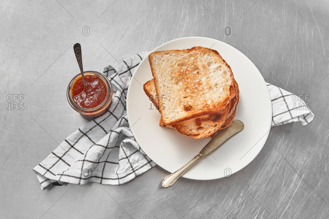 Healthy breakfast or snack with fresh grilled toasts and glass jar of sweet delicious jam on a light grey concrete background, served textile napkin, copy space.