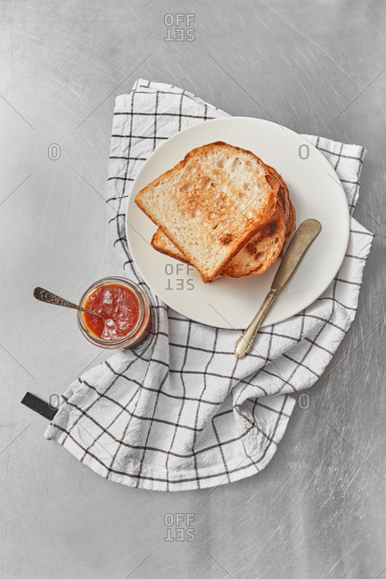 Top view breakfast set with freshly baked stack of toasts and glass jar of sweet delicious jam on a light grey stone background, served textile napkin, copy space.