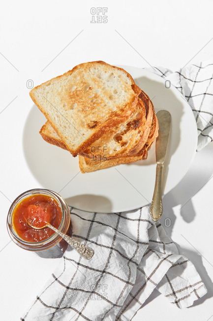 Healthy breakfast or snack with freshly baked toasts and glass jar of sweet apricot jam on a light grey concrete background, served textile napkin, copy space.