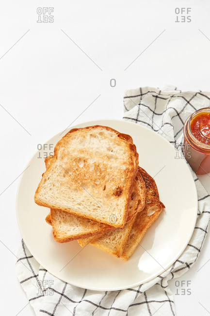 Healthy snack or breakfast with freshly baked toasts and glass jar of sweet apricot jam on a light grey concrete background, served textile napkin, copy space.