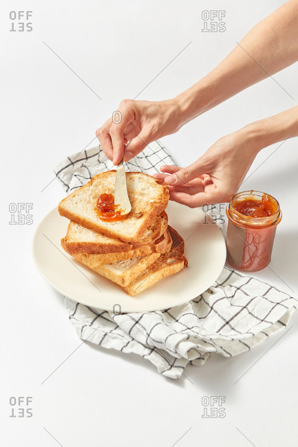 Process of preparing healthy breakfast by woman hand from freshly baked toasts and sweet apricot jam on a light grey concrete background, served textile napkin, copy space.