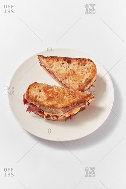 Freshly cooked homemade grilled hot toasts with ham and cheese on a ceramic plate on a white background with soft shadows, copy space.