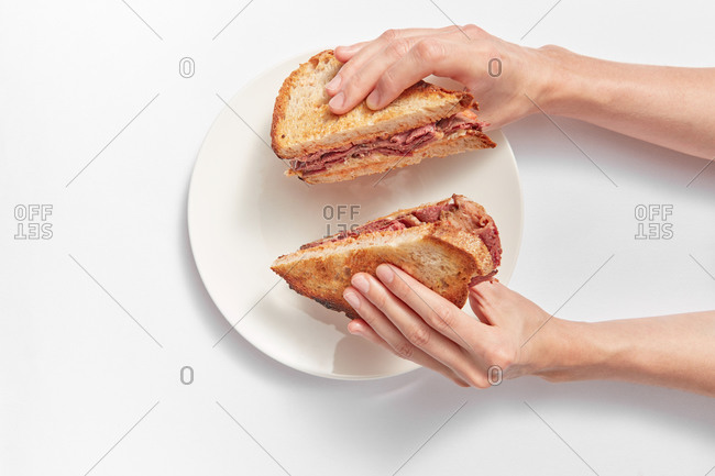Two homemade freshly cooked healthy sandwiches with ham and cheese in a woman's hands above ceramic plate on a white background, copy space.