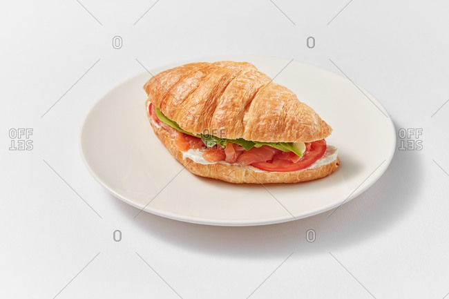 Freshly cooked homemade sandwich with natural salmon and tomatoes on a ceramic plate on a white background with soft shadows, copy space.