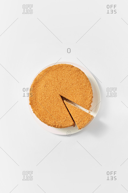 Top view of the whole homemade freshly baked honey cake with cut piece of delicious sweet dessert on a ceramic plate on white background, copy space.