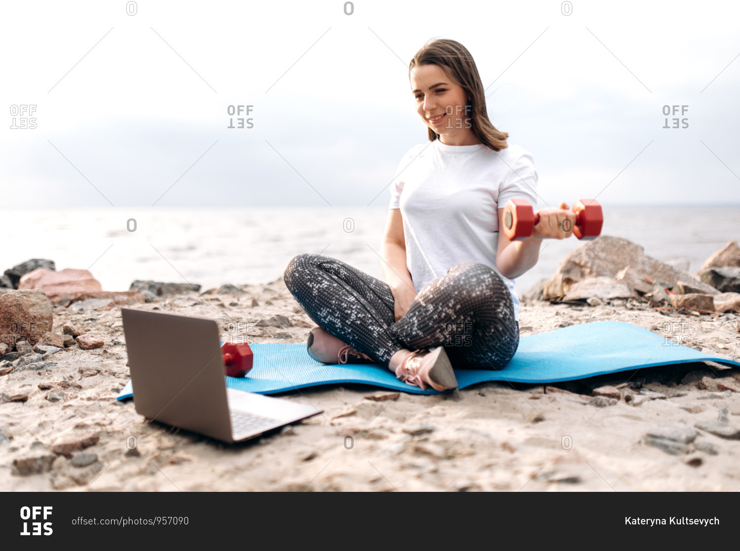 Fitness workout by video tutorial. A young girl does\
exercises with dumbbells while sitting on a mat and watches a video\
fitness lesson during a workout in nature stock photo -\
OFFSET