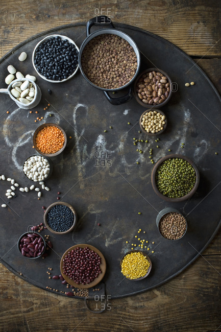 Bowls with various beans and lentils on rustic baking sheet