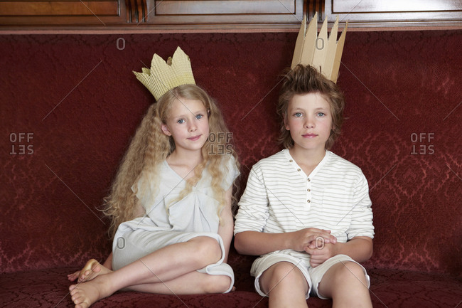 Boy and girl sitting on a couch wearing cardboard crowns