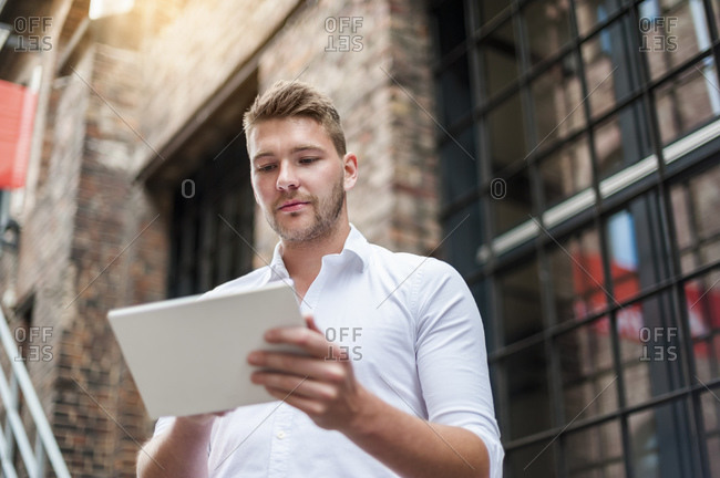 Young businessman using tablet at a brick building