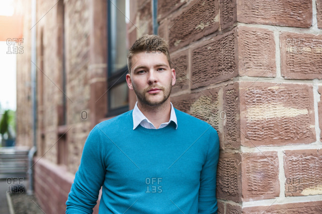 Portrait of a young businessman leaning against a brick building