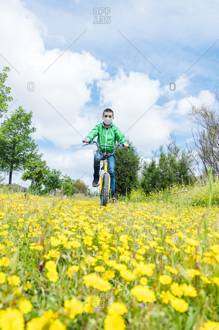 Full length of boy wearing face mask cycling over yellow flowers on field against sky