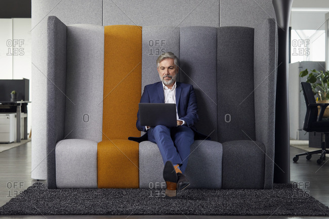 Mature businessman sitting on couch in office using laptop