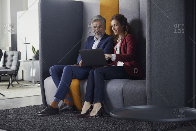 Businesswoman and businessman sitting on couch in office sharing laptop