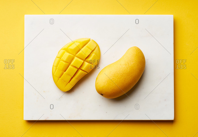 Sliced yellow mango on marble cutting board and yellow background. Top view