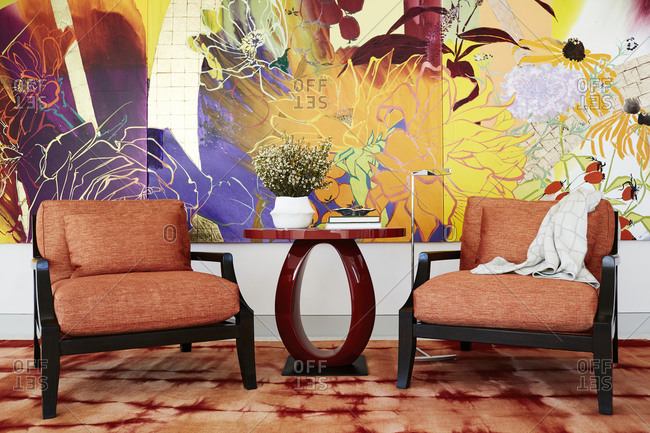 Paradise Valley, Arizona - July 10, 2019: Two cushioned chairs beside red side table in front of large colorful painting