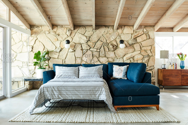 June 1, 2020: Blue sectional sofa with pullout bed in a room with exposed beam ceiling and stone wall
