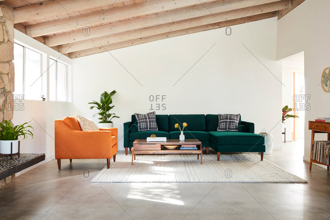 June 1, 2020: Green velvet sectional sofa and orange chair in a room with exposed beam ceiling