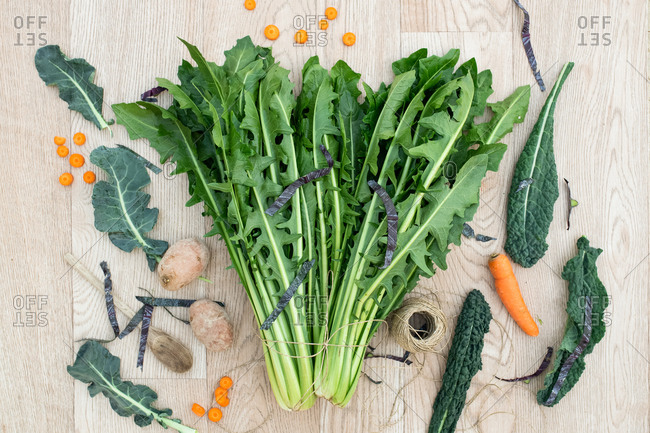 High angle close up of freshly picked green leafy vegetables and carrots on wooden table.