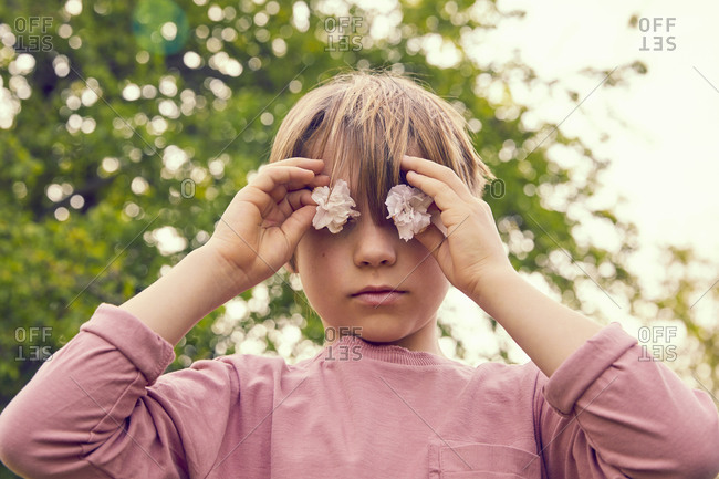 Portrait of smiling boy standing outdoors, looking at camera through pink blossoms.