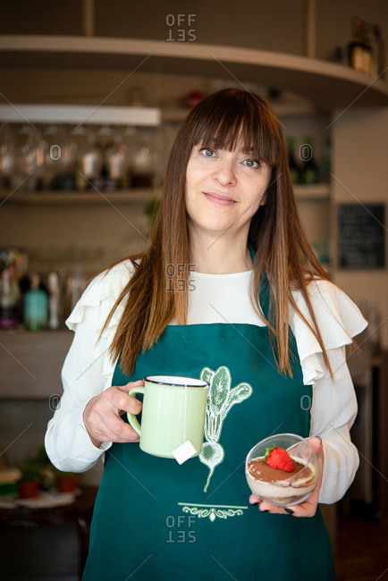 A woman waitress in a vegan cafe, carrying a mug and a dessert with a large strawberry.