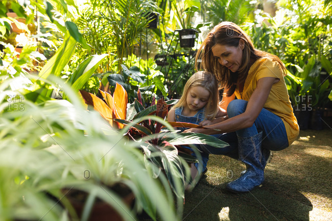 A Caucasian woman and her daughter enjoying time together in a sunny garden, looking at plants together and touching their leaves and flowers