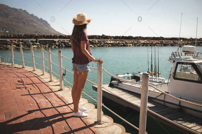 A teenage Caucasian girl, wearing a straw hat, enjoying her time on a promenade, on a sunny day,  leaning on a barrier, looking away