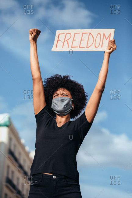 Afro woman protesting at a rally for racial equality. She is raising fist holding a sign with the word "Freedom". Black Lives Matter.
