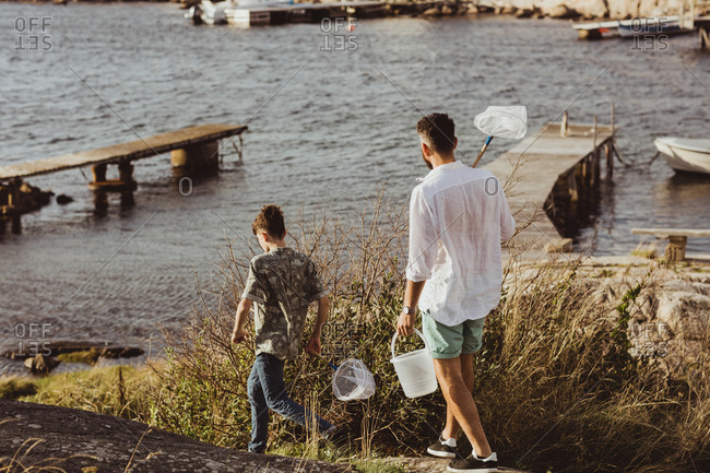 Rear view of father and son walking with fishing net by sea during weekend