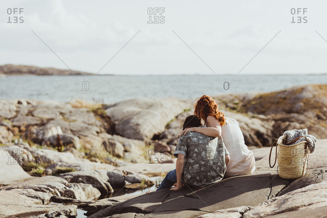 Rear view of mother and son bonding while sitting over rocky land during sunny day