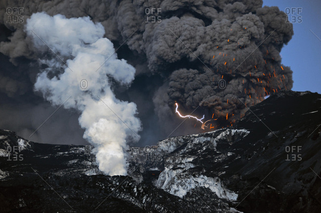 A flash of lightning in the ash cloud from the Eyjafjallajoekull Volcano while it ejects magma, lava flow in front of the glacier producing a water vapor cloud, Eyjafjallajoekull, Iceland, Europe