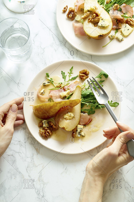Female hands holding a plate of pear salad with walnuts, prosciutto, arugula and blue cheese. Dinner appetizer on marble table