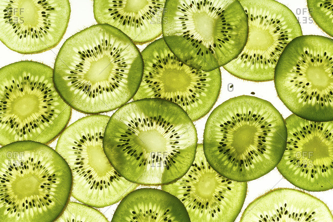 Backlit kiwi fruit slices on white background. Top view texture
