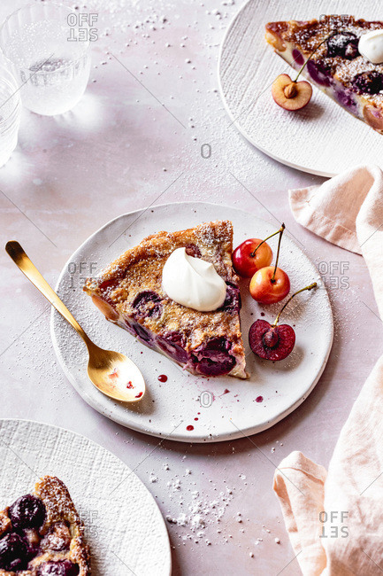 A slice of cherry clafoutis served with fresh cherries and creme fraiche.