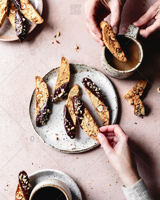 Hands picking up pieces of chocolate dipped hazelnut biscotti.