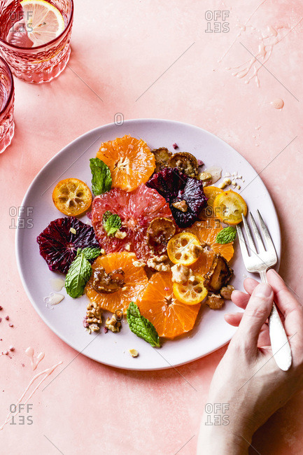 Citrus fruit salad with rosewater, dates, and walnuts and a hand held fork.