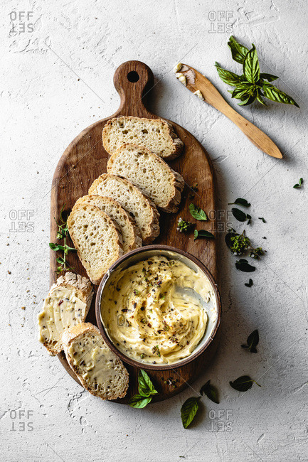 Garlic and herb butter with a sliced baguette on a wooden serving board.