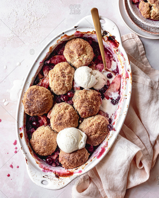 Cranberry apple cobbler in a baking dish with scoops of ice cream.