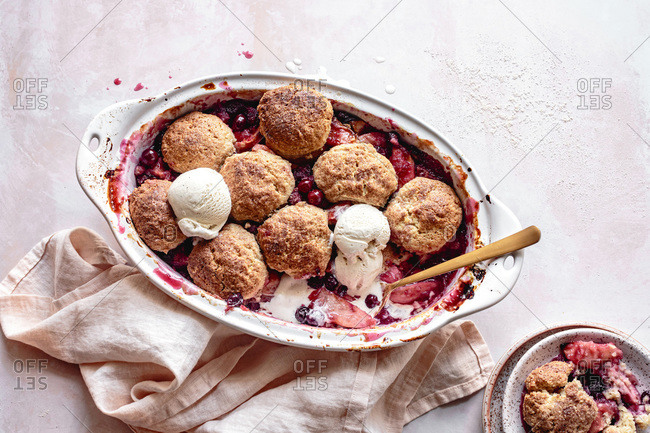 Cranberry apple cobbler in a baking dish with scoops of ice cream.