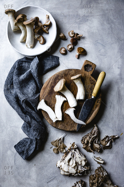 Trumpet and maitake mushrooms on a wooden cutting board.