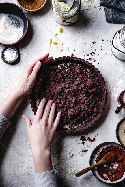 Hands preparing a chocolate tart crust.