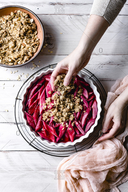 Oat crumble in a woman's hand sprinkled over rhubarb in baking dish.