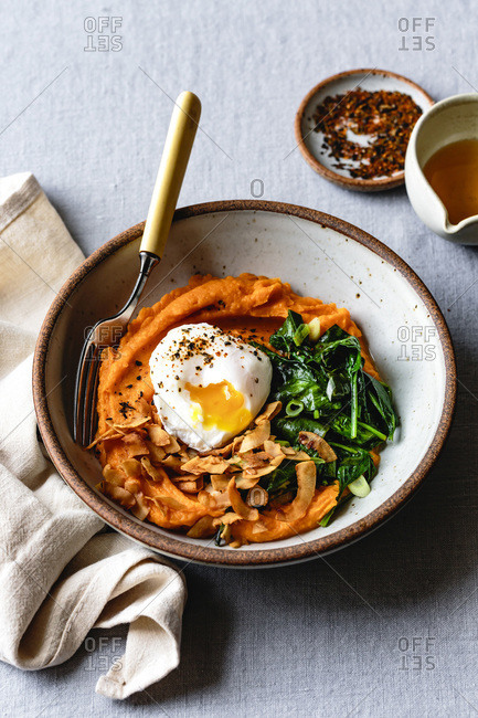 Closeup view of a sweet potato breakfast bowl with coconut bacon, spinach and poached egg.