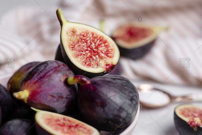 Close up of halved and whole purple figs in a bowl with a pink and white striped napkin and rose gold spoon full of sugar in the blurred background